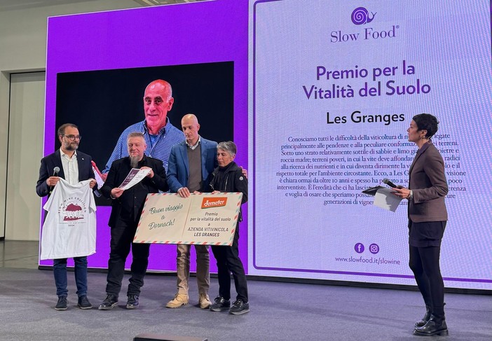 Liana Grange riceve il premio sul palco di Slow Wine; sullo sfondo, il volto di Gualtiero Crea